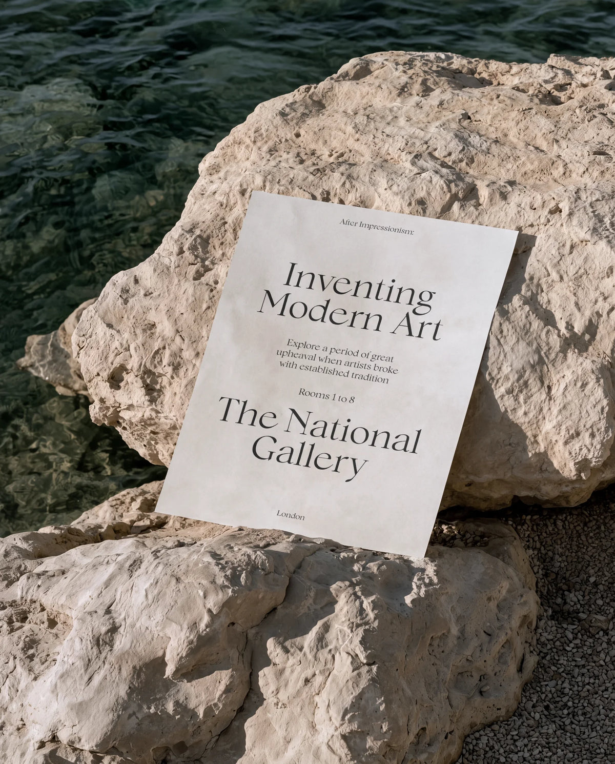National Gallery exhibition poster using Chiffon typography, photographed against pale coastal rocks.