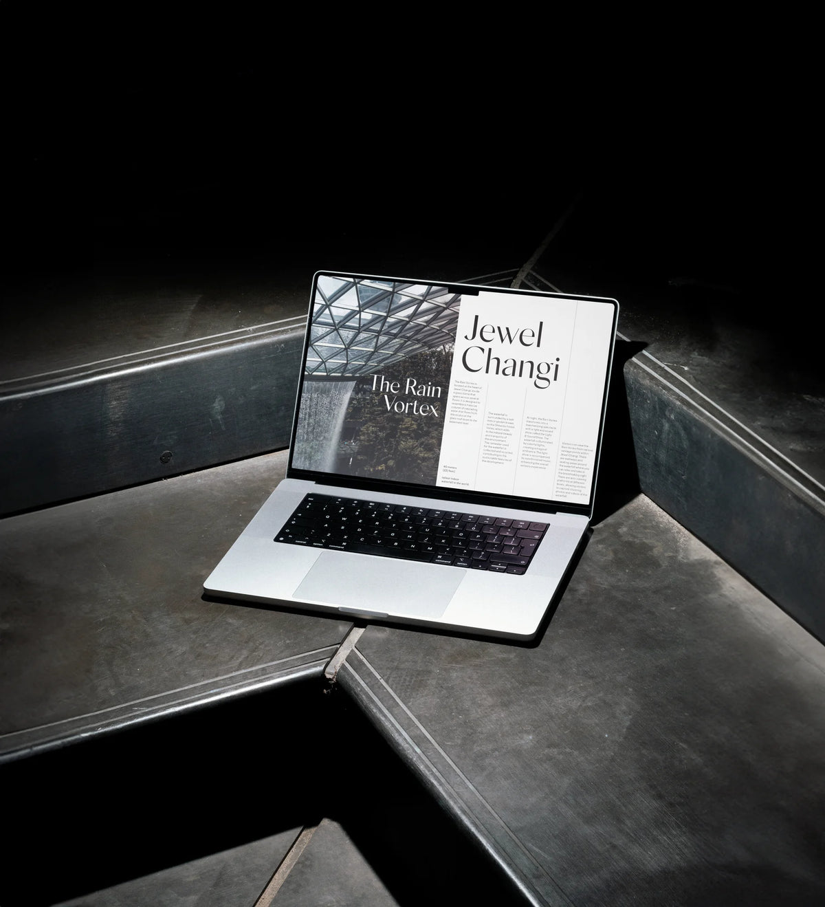 Laptop displaying a Jewel Changi editorial web layout using Silk Sans typography on a dark industrial surface.