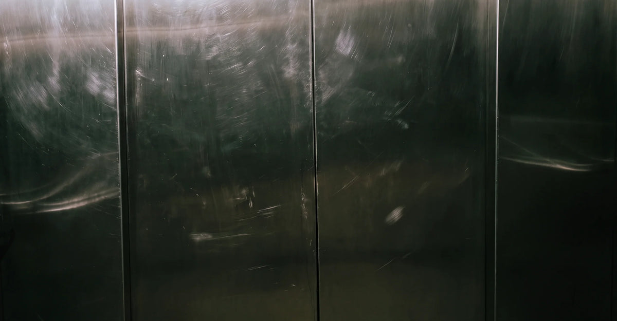 Close-up of dark brushed metal with scratches and soft reflections, used as a visual background for Silk Sans.