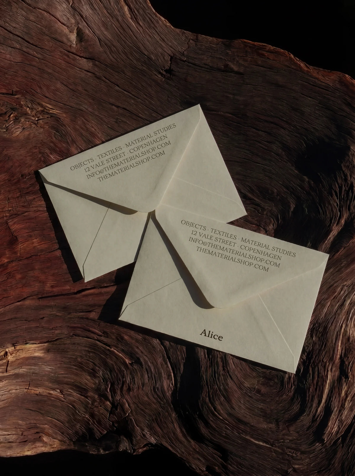 Cream envelopes with refined editorial typography using Velour Raw, photographed on dark textured wood.