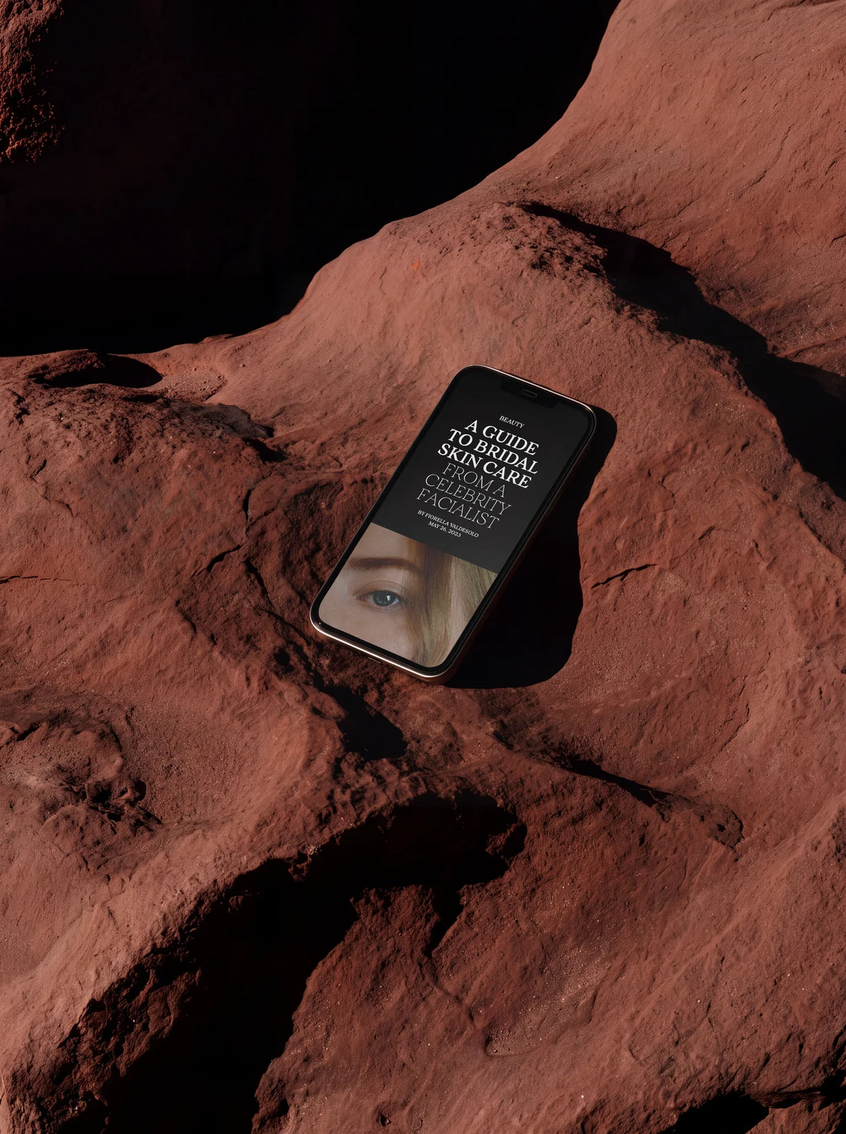 Smartphone displaying a beauty editorial layout using Velour Raw typography, photographed on warm red rock.