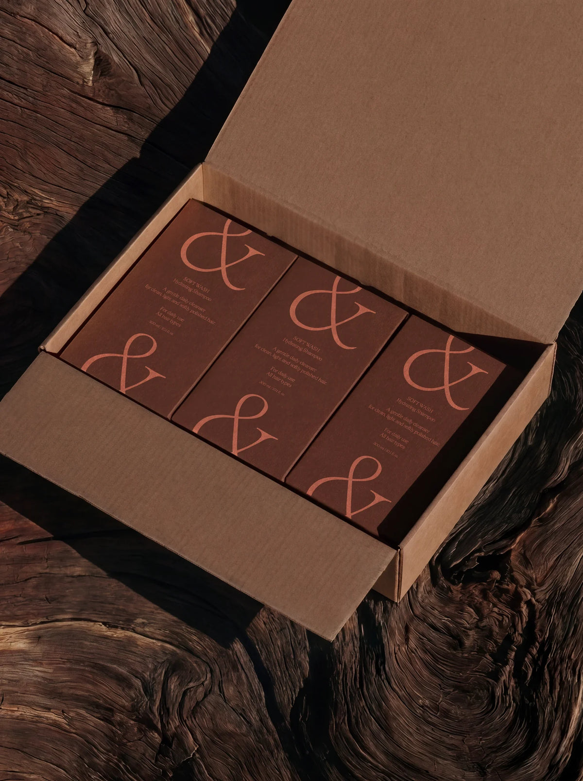 Brown product boxes featuring oversized ampersand typography set in Velour Raw, photographed inside an open cardboard box.