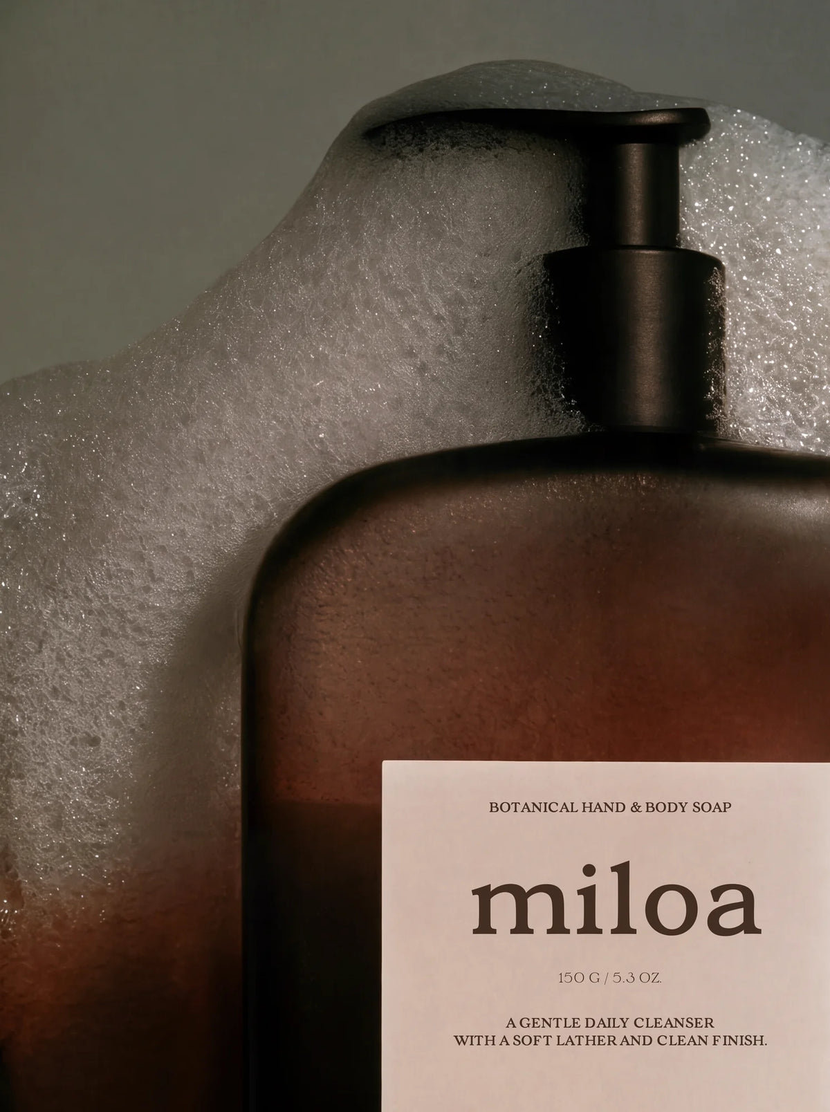 Brown botanical hand and body soap bottle labeled Miloa with typography set in Velour Raw and surrounded by soft foam.